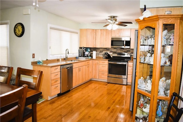 kitchen featuring light wood-style flooring, a sink, decorative backsplash, light brown cabinetry, and stainless steel appliances