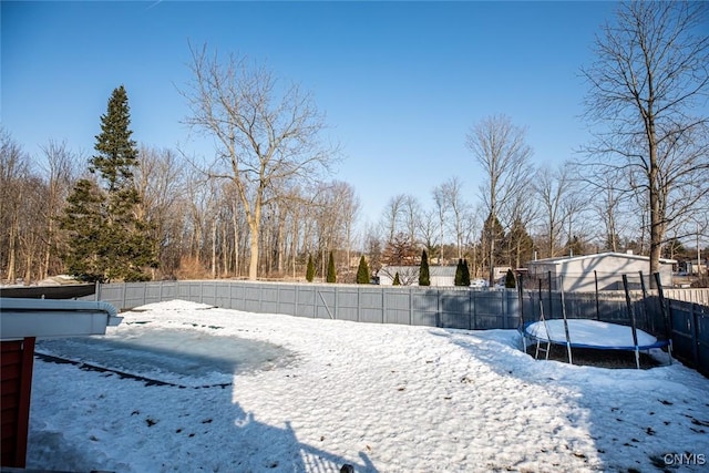 yard layered in snow featuring a trampoline and a fenced backyard