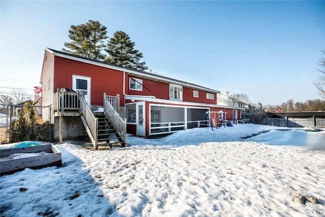 snow covered rear of property with stairway, fence, and a sunroom