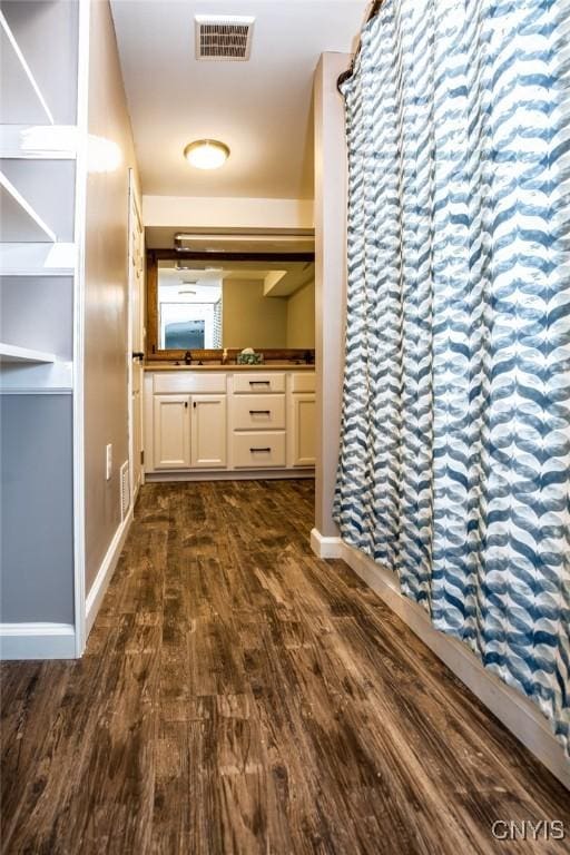 corridor with a sink, dark wood-style floors, visible vents, and baseboards