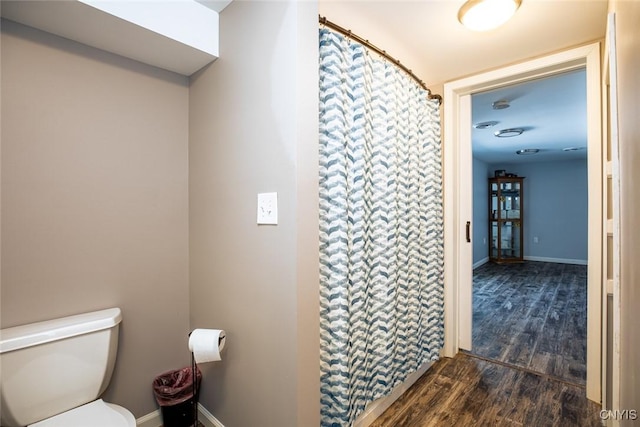 bathroom with curtained shower, toilet, wood finished floors, and baseboards