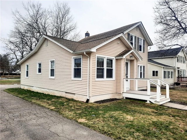 view of front of home with a front lawn, a chimney, and a shingled roof