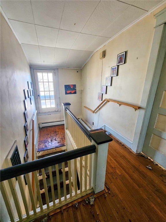 staircase with a baseboard heating unit, ornamental molding, and hardwood / wood-style flooring