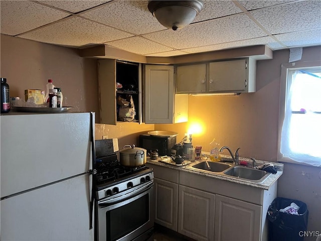 kitchen featuring a sink, a drop ceiling, stainless steel gas range, and freestanding refrigerator