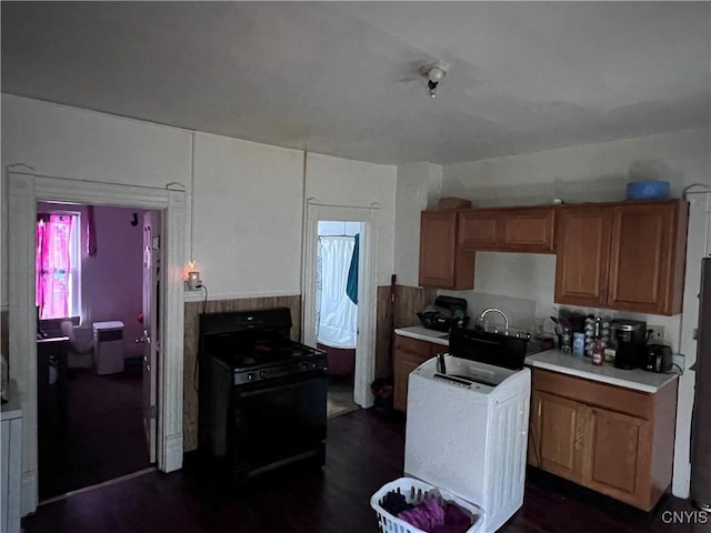 kitchen featuring black range with gas cooktop, brown cabinets, washer / clothes dryer, and light countertops