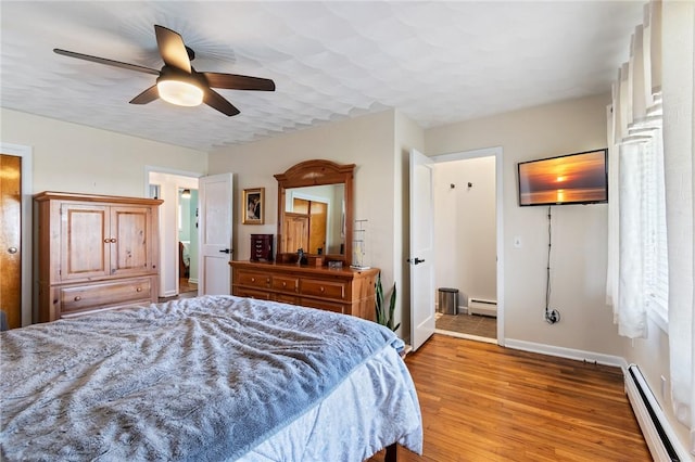 bedroom featuring light wood finished floors, baseboard heating, a ceiling fan, and baseboards