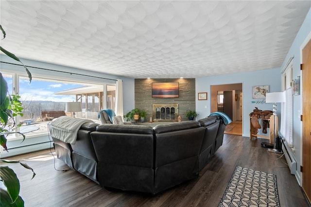 living room with baseboard heating, a brick fireplace, and dark wood-type flooring