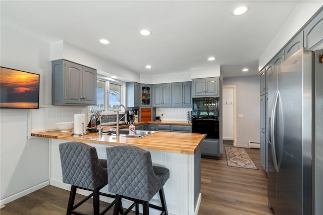 kitchen featuring gray cabinetry, a breakfast bar area, a peninsula, black appliances, and a sink