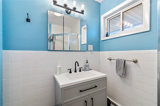 bathroom with a wainscoted wall, tile walls, a stall shower, and vanity