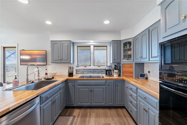 kitchen featuring gray cabinetry, butcher block counters, wood finished floors, black appliances, and a sink