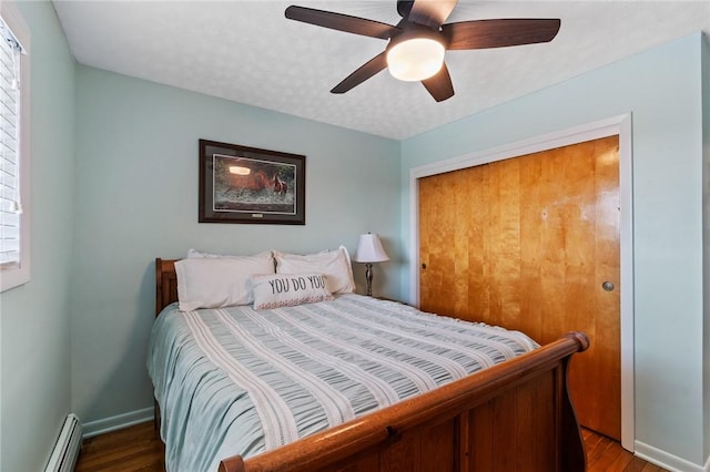 bedroom featuring a baseboard heating unit, wood finished floors, baseboards, and a textured ceiling