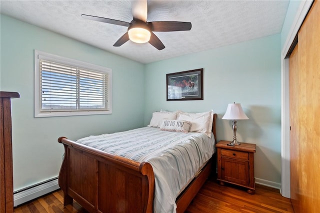 bedroom featuring a baseboard heating unit, baseboards, a closet, dark wood-style floors, and a textured ceiling