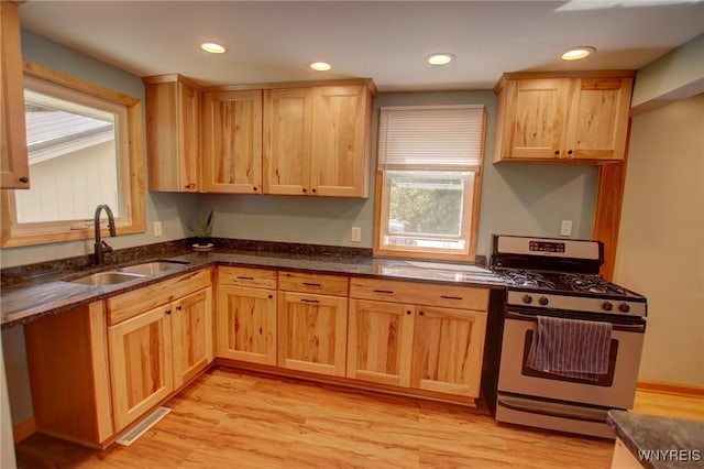 kitchen with stainless steel range with gas stovetop, light brown cabinets, visible vents, and a sink