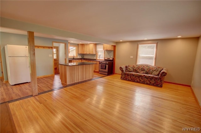 kitchen with light brown cabinets, gas stove, freestanding refrigerator, light wood-style floors, and dark countertops