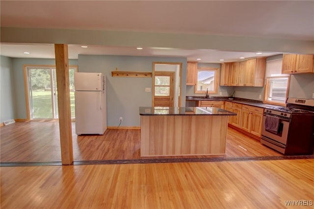 kitchen with stainless steel gas stove, a wealth of natural light, freestanding refrigerator, and light wood-style floors