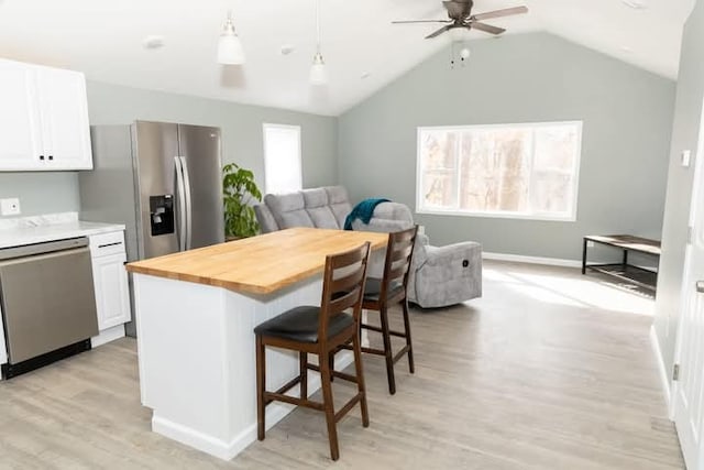 kitchen featuring a kitchen bar, open floor plan, stainless steel appliances, white cabinets, and butcher block counters