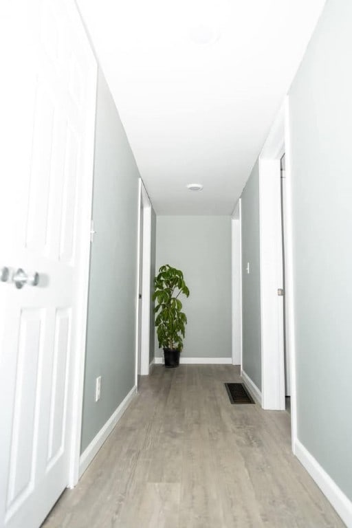 hall featuring wood finished floors, visible vents, and baseboards