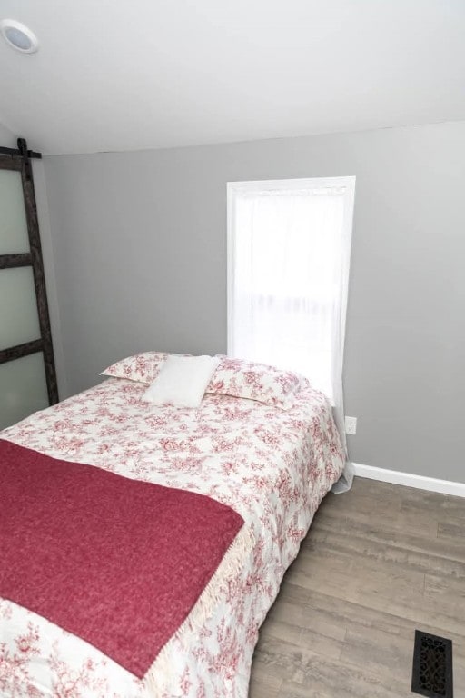 bedroom featuring a barn door, visible vents, baseboards, and wood finished floors