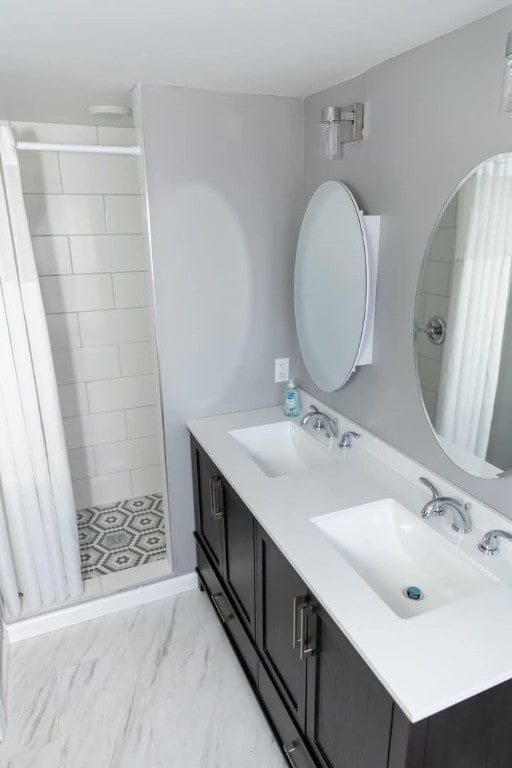 bathroom featuring a shower stall, double vanity, marble finish floor, and a sink