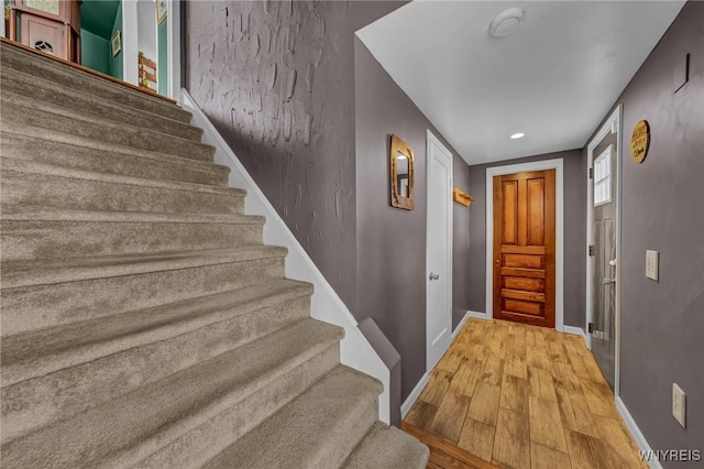 foyer featuring baseboards, stairs, and light wood finished floors