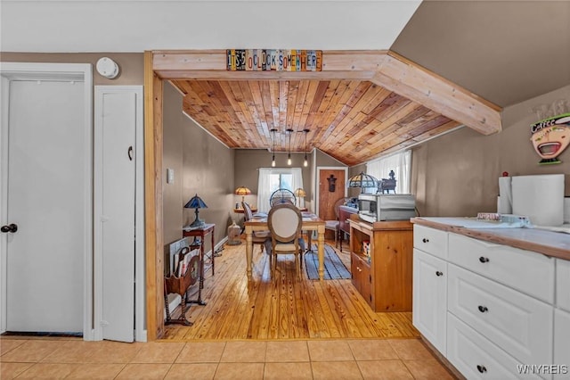 kitchen featuring stainless steel microwave, vaulted ceiling, light tile patterned floors, wooden ceiling, and white cabinets