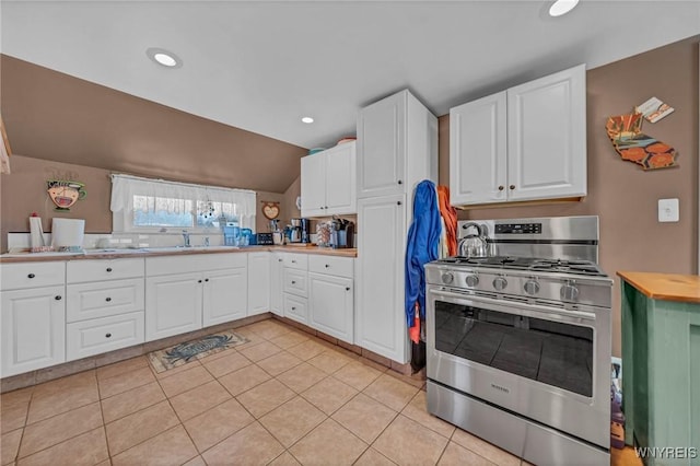 kitchen featuring lofted ceiling, a sink, white cabinets, light tile patterned flooring, and gas range