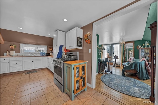 kitchen with a sink, open floor plan, white cabinetry, light countertops, and stainless steel range with gas stovetop