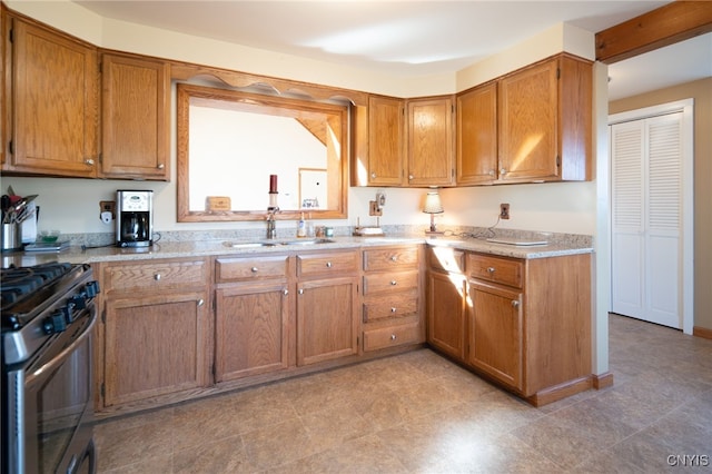 kitchen with a sink, light stone counters, brown cabinets, and stainless steel gas range oven