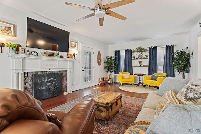 living room featuring a fireplace with raised hearth, ceiling fan, and wood finished floors