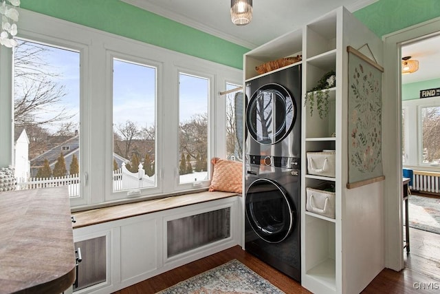 laundry area with laundry area, crown molding, stacked washer / drying machine, and dark wood-type flooring