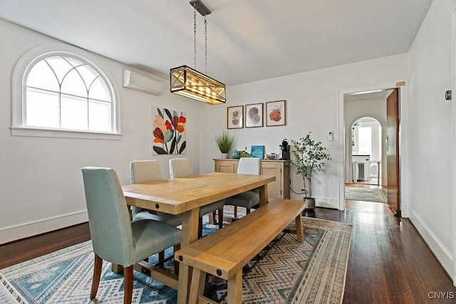 dining space featuring dark wood finished floors, arched walkways, a wall mounted air conditioner, and baseboards