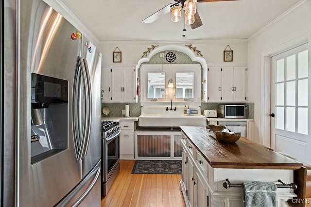 kitchen featuring butcher block countertops, backsplash, white cabinetry, stainless steel appliances, and light wood finished floors