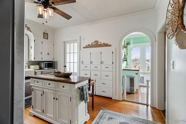 kitchen featuring stainless steel microwave, light wood-style floors, a ceiling fan, and white cabinetry