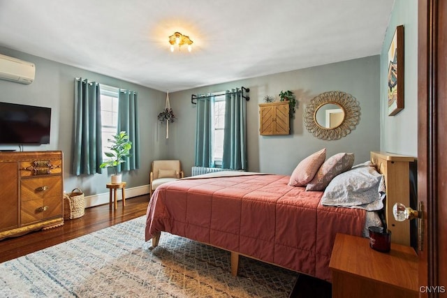 bedroom featuring a wall mounted air conditioner, baseboards, and wood finished floors