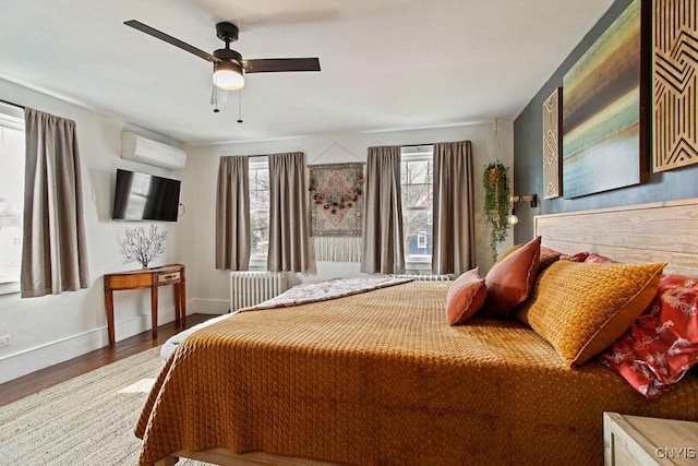 bedroom with an AC wall unit, wood finished floors, radiator, baseboards, and ceiling fan