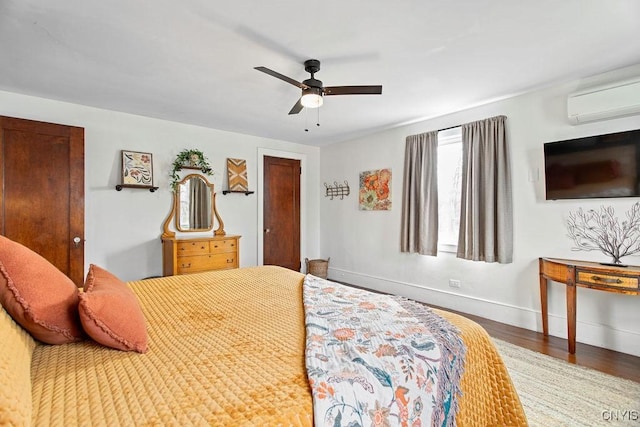 bedroom with ceiling fan, a wall mounted AC, baseboards, and wood finished floors