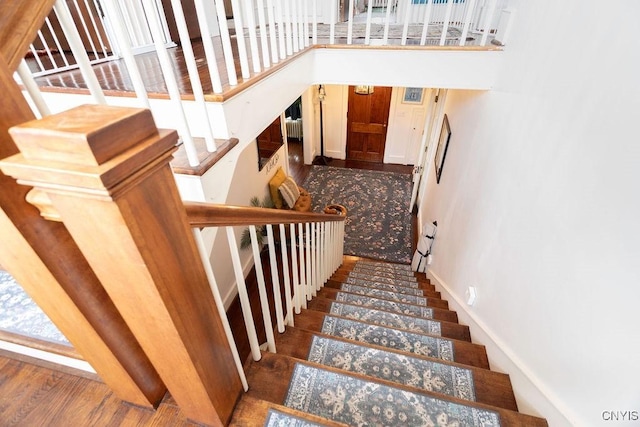 staircase with baseboards, wood finished floors, and a towering ceiling