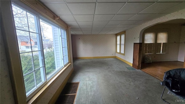 empty room with visible vents, baseboards, wallpapered walls, arched walkways, and a drop ceiling