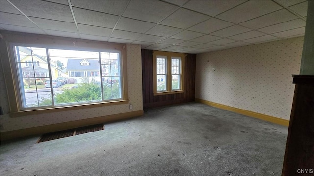 empty room featuring baseboards, a drop ceiling, wallpapered walls, and carpet