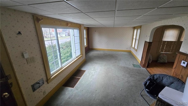 unfurnished room featuring visible vents, a drop ceiling, arched walkways, wallpapered walls, and baseboards