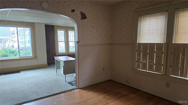 unfurnished room with wallpapered walls, wood finished floors, baseboards, and arched walkways