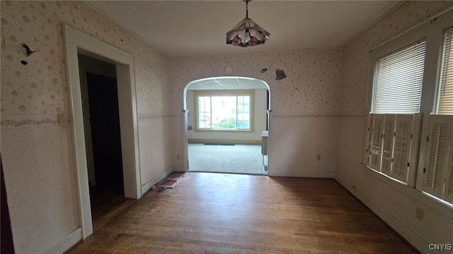 interior space featuring arched walkways, wallpapered walls, baseboards, and wood finished floors