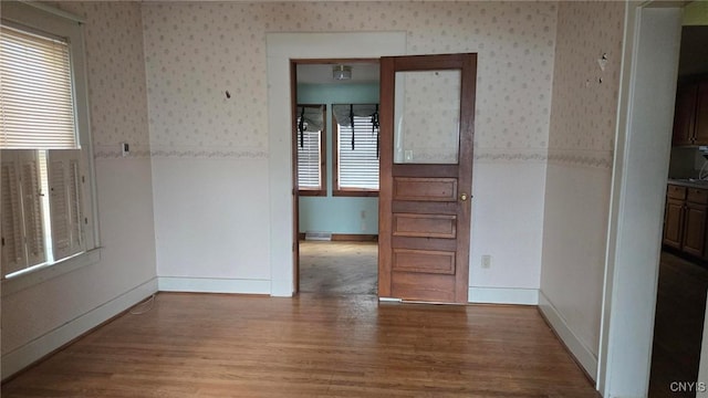 empty room featuring visible vents, baseboards, wood finished floors, and wallpapered walls