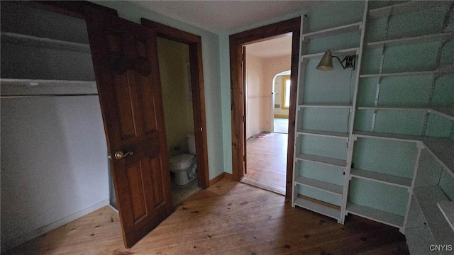 hall with baseboards, wood-type flooring, and arched walkways