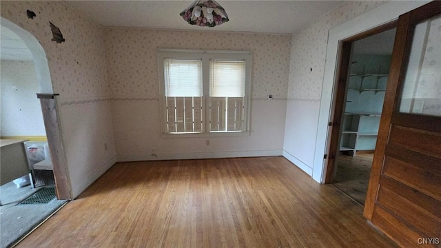 empty room featuring wallpapered walls, wood finished floors, arched walkways, and wainscoting