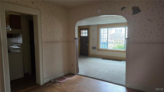 entrance foyer featuring baseboards, arched walkways, wood finished floors, and wallpapered walls