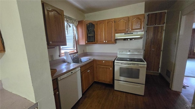 kitchen with dark wood-type flooring, under cabinet range hood, brown cabinets, white appliances, and a sink