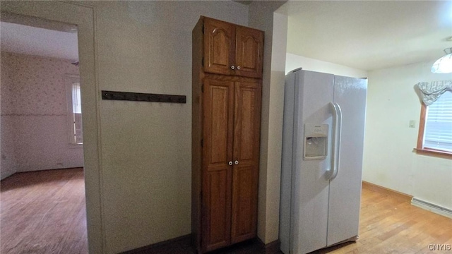 kitchen with baseboard heating, light wood finished floors, brown cabinetry, and white fridge with ice dispenser