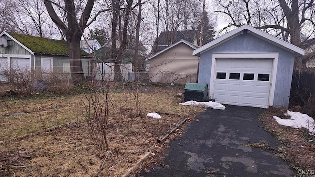 view of side of property with aphalt driveway, a detached garage, an outbuilding, and fence