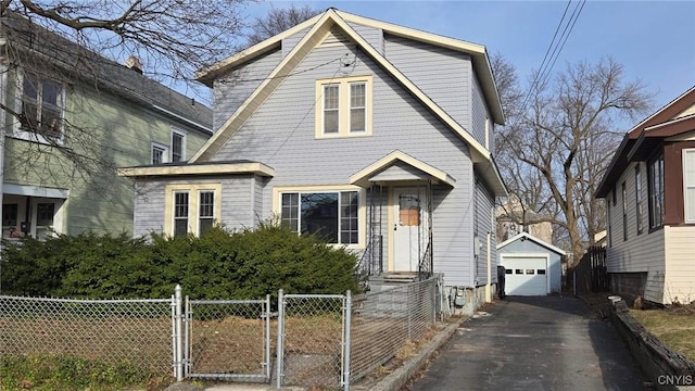 view of front of property featuring an outbuilding, a gate, aphalt driveway, a fenced front yard, and a detached garage